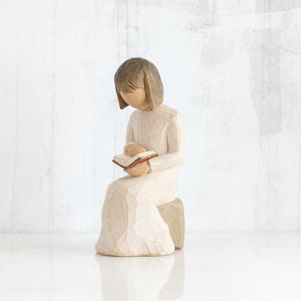 Wisdom by Willow Tree. Figure in cream dress seated on a gray rock, reading a book