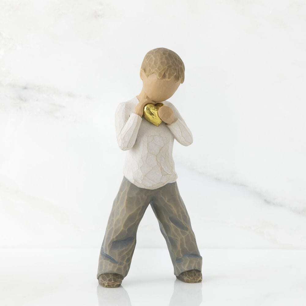 Heart of Gold by Willow Tree. Standing boy figure in cream shirt and blue jeans, holding gold-leaf heart with both hands to his chest