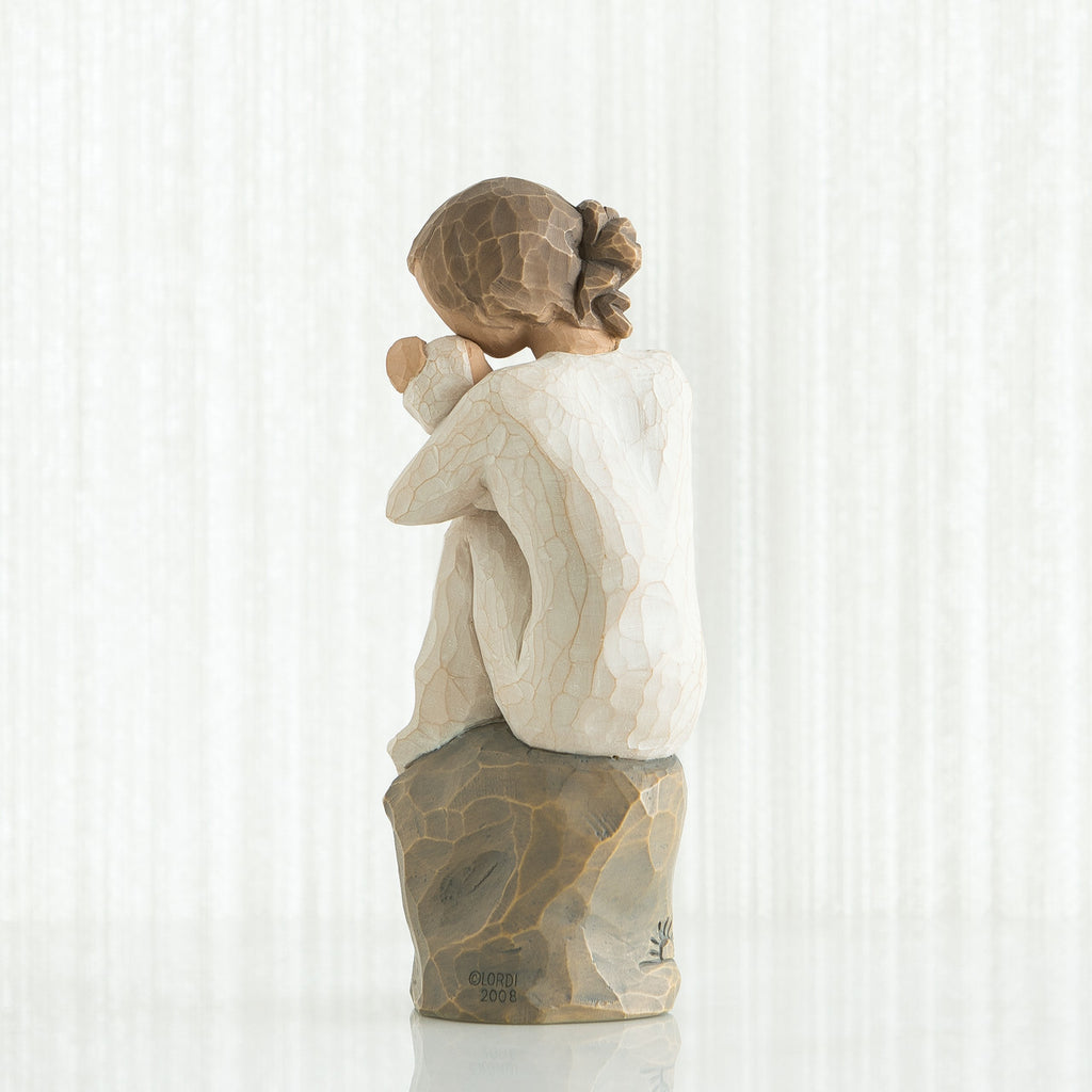 Figure in cream dress, seated on a gray rock, holding newborn baby wrapped in cream blanket