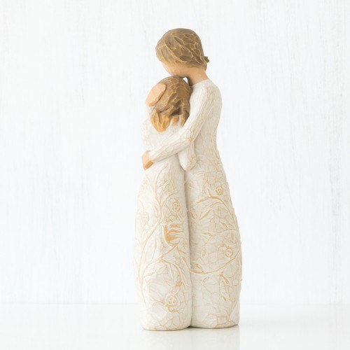 Figure of standing older woman embracing younger girl, both in cream dresses carved with intertwined vines and leaves