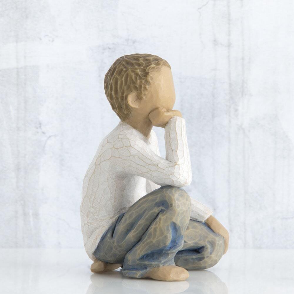 Figure of half-kneeling boy in cream shirt and blue jeans, with hand under chin