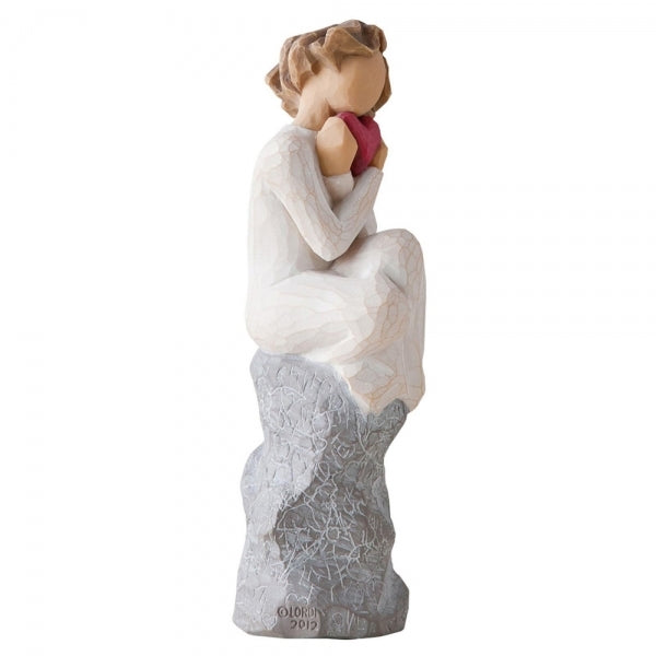 Female figure in cream dress, seated on a gray rock, with knees drawn up to chest, holding red heart up to face. Rock etched with words and symbols of love