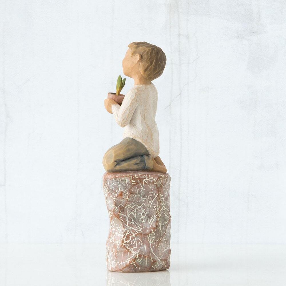 Figure of small boy in cream shirt and blue jeans holding a small green plant in terracotta pot, kneeling on tall red rock, etched with words and imagery of earth, nature and puzzle pieces