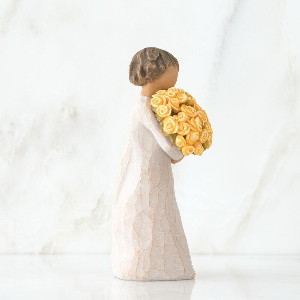 Standing figure in cream dress, holding large bouquet of yellow roses in her arms