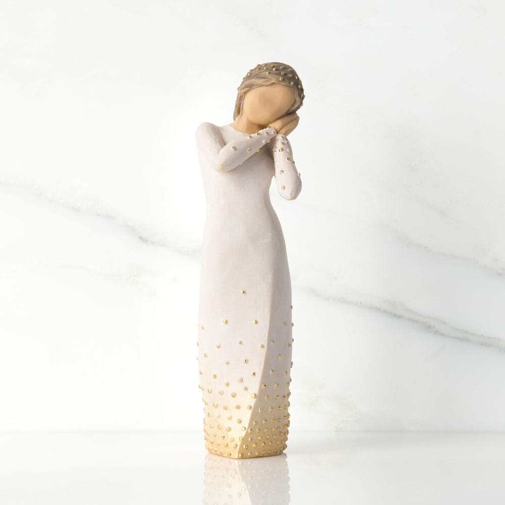 Standing figure in cream dress, holding up arms to face in wistful gesture. Bottom of dress embellished with gold and gold-leaf dots